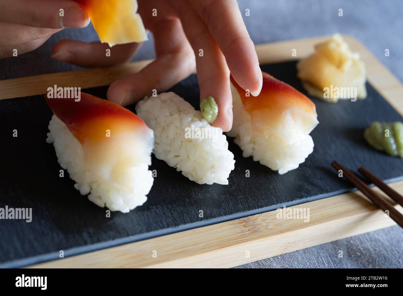 Femme asiatique préparant des sushis - placer du wasabi sur du riz à sushi avec des palourdes crues de surf (japonais : Hokkigai ou Ubaggai) comme collation maison de style japonais Banque D'Images
