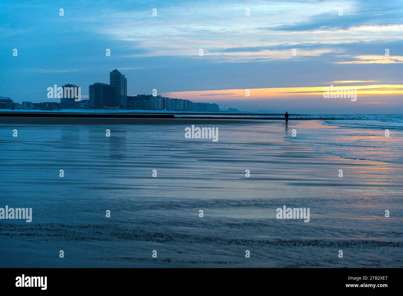 Un homme en vêtements d'hiver marchant au coucher du soleil sur la plage d'Ostende avec Skyline par temps de neige, Flandre, Belgique. Banque D'Images