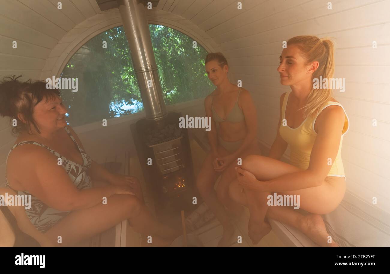 Quatre femmes assises dans un sauna finlandais en baril, souriant et appréciant la chaleur Banque D'Images