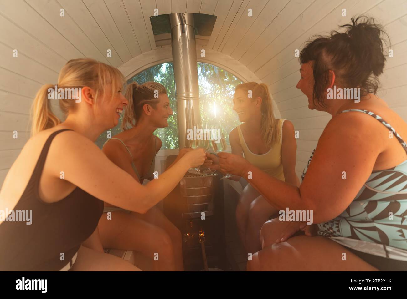 Quatre femmes grimpant avec des verres dans un sauna finlandais en baril, riant et profitant de leur temps Banque D'Images