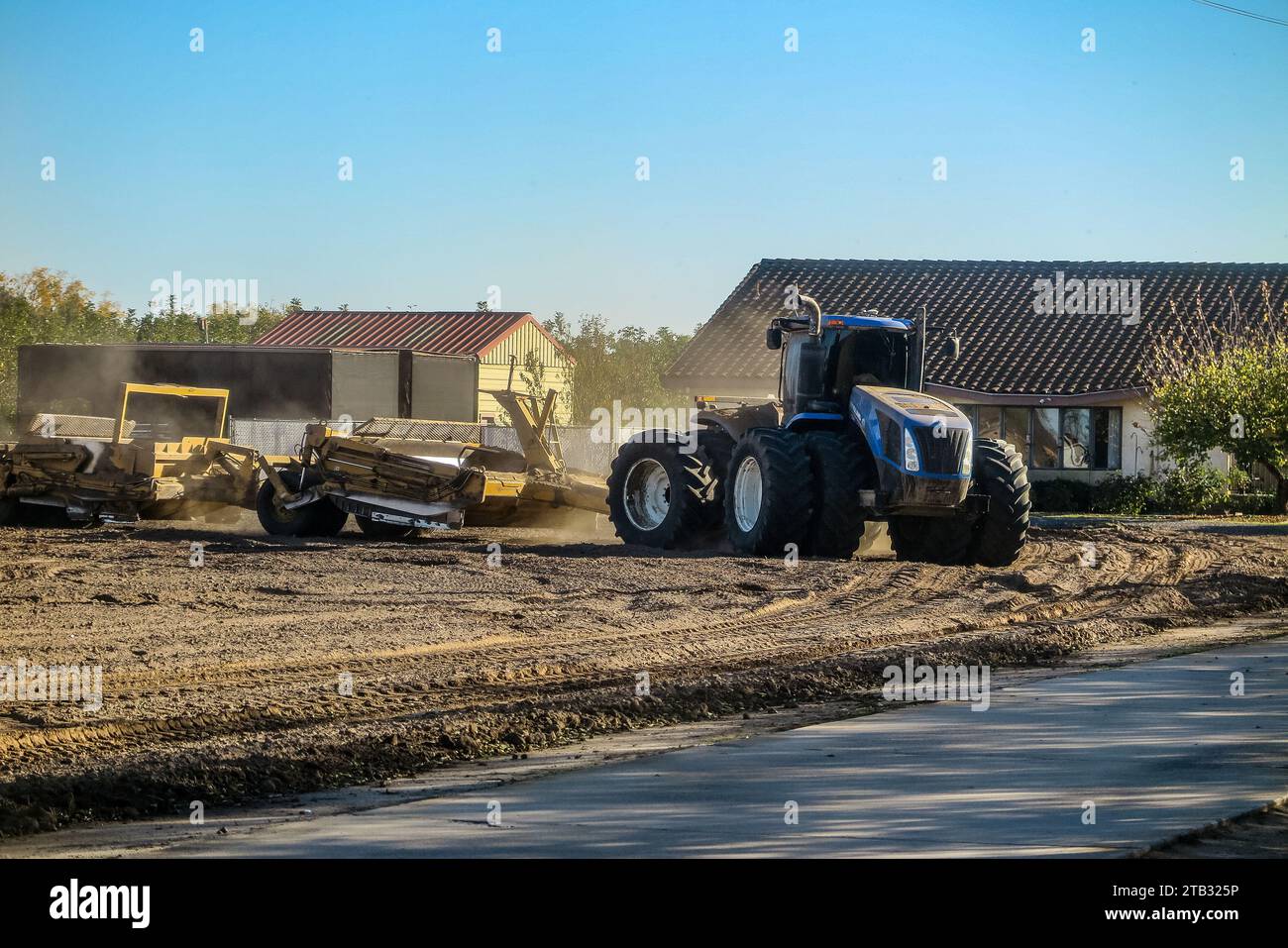 Un tracteur tire des grattoirs guidés au laser pour niveler un ancien verger de noyer afin de le préparer à planter de nouveaux arbres dans la vallée centrale de Californie, aux États-Unis Banque D'Images