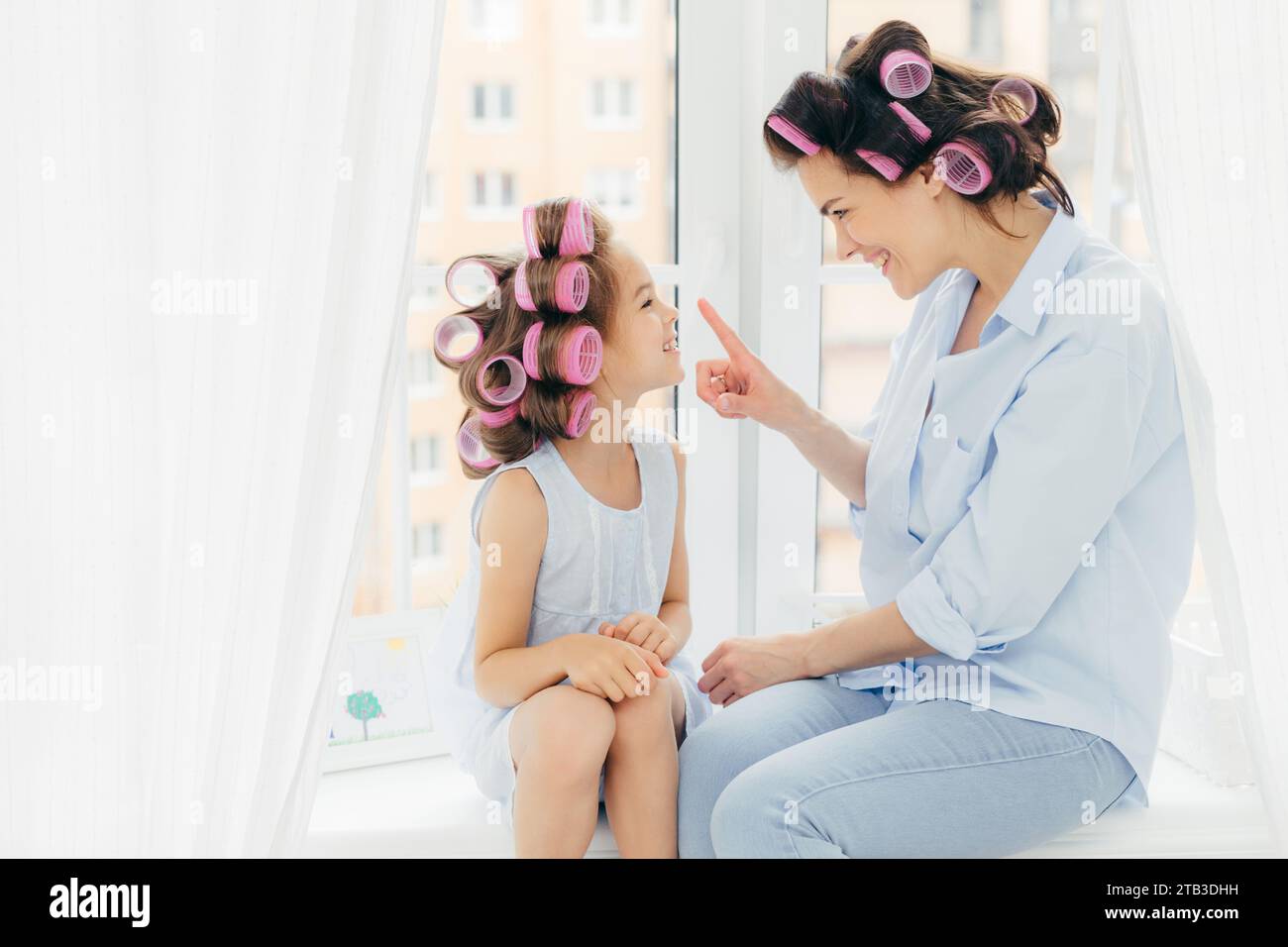 Mère et fille avec des rouleaux de cheveux, profitant d'une journée de beauté ludique. Banque D'Images