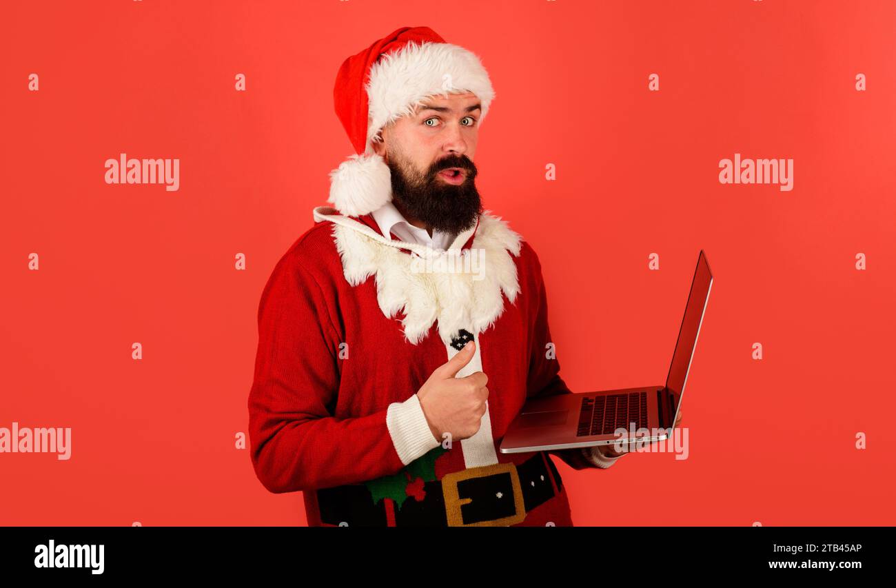 Surpris Père Noël avec ordinateur portable montrant le pouce vers le haut. Site de commerce électronique, vacances de Noël, achats en ligne, vente e-commerce. Achetez des cadeaux de Noël en ligne Banque D'Images