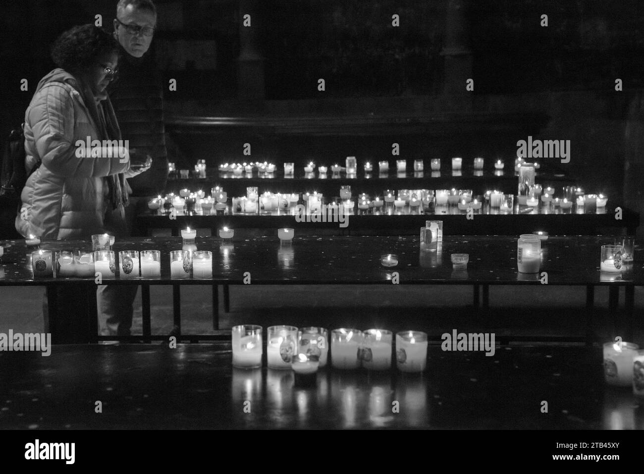 Metz, France - 26 décembre 2022 : couple d'âge moyen allumant des bougies dans la cathédrale Saint-Étienne le lendemain des vacances de Noël. Photo historique noir et blanc. Banque D'Images