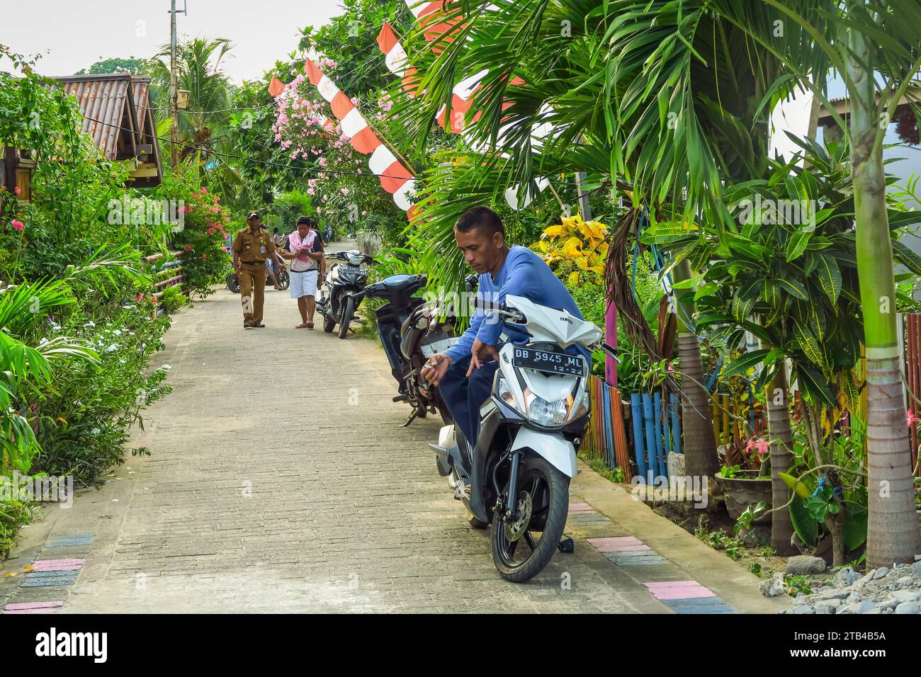 L'artère principale avec homme et scooter sur cette île de vacances sans voiture populaire et destination de plongée sous-marine. Île de Bunaken, Sulawesi du Nord, Indonésie Banque D'Images