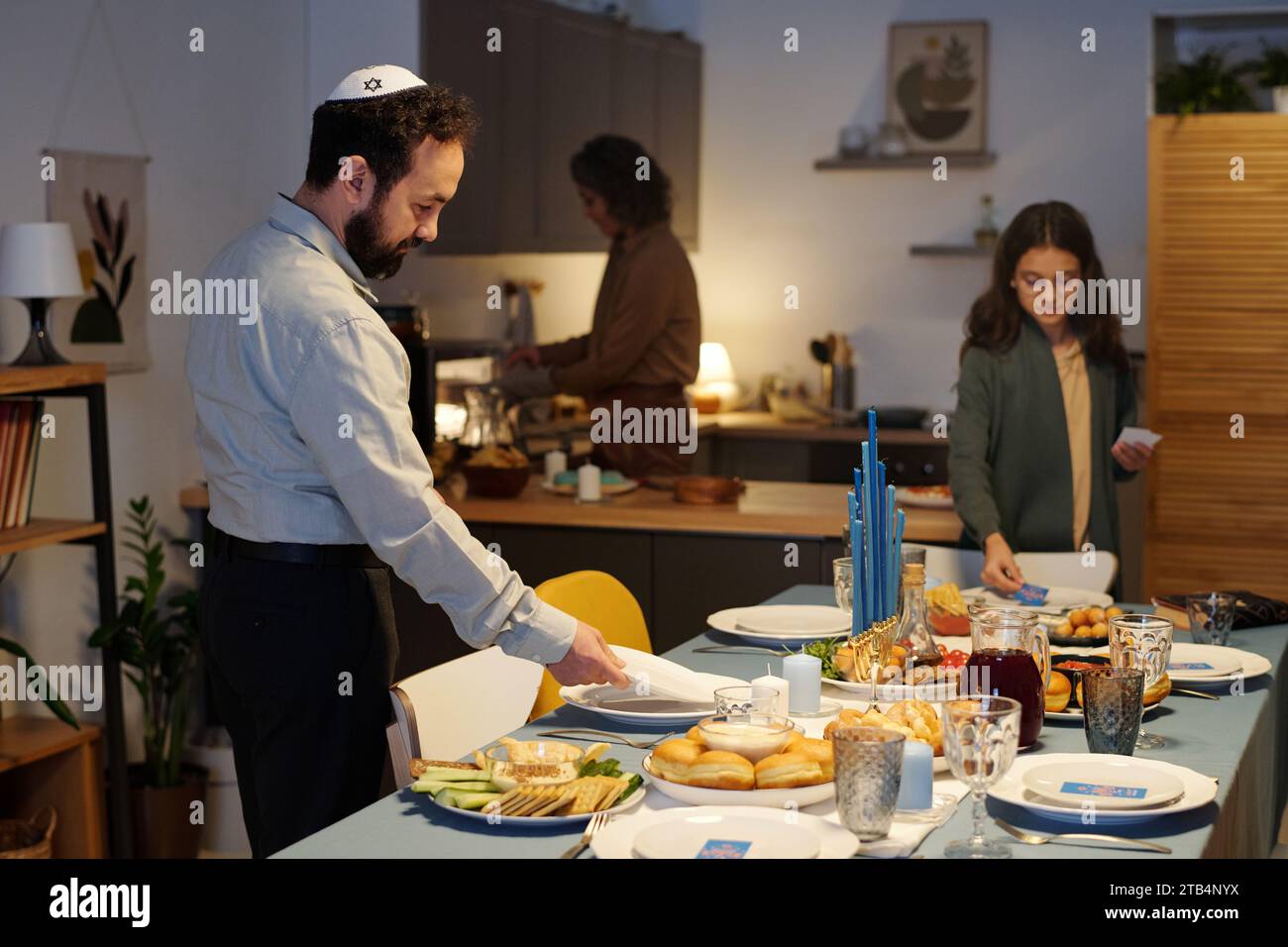 Vue latérale de l'homme juif barbu dans la table de service Skullcap pour le dîner tout en se préparant à la célébration de Hanoukka avec sa famille à la maison Banque D'Images