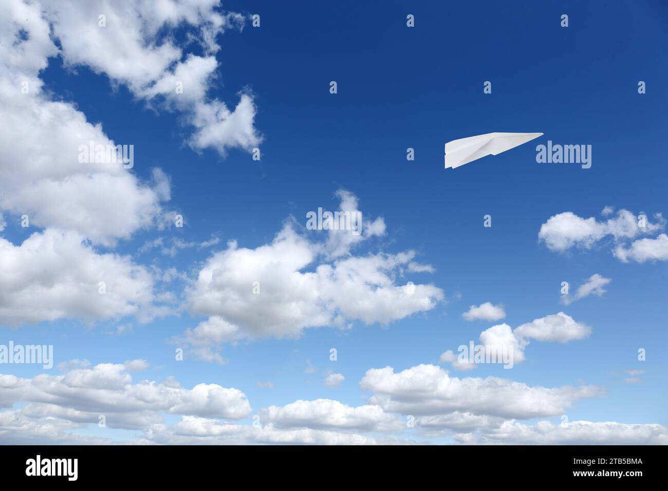 Avion en papier blanc volant dans le ciel bleu avec des nuages Banque D'Images