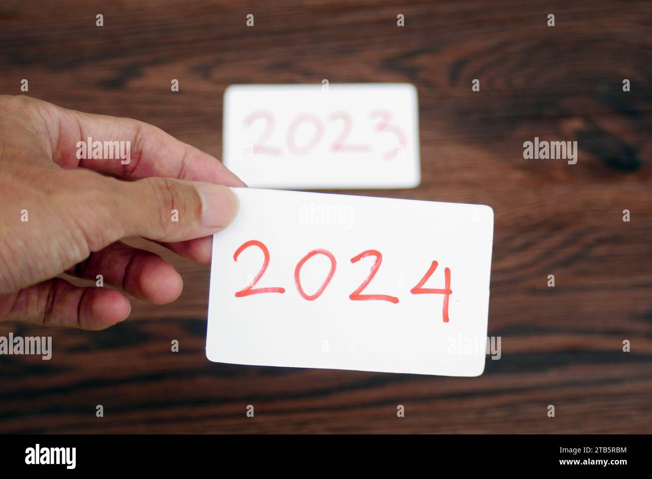 La main prend la carte 2024 en laissant la carte 2023 derrière elle