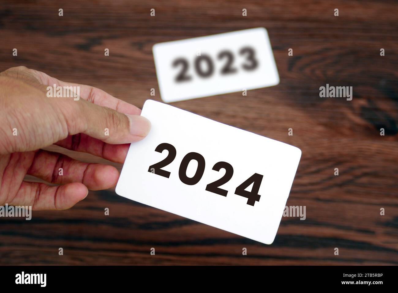 La main prend la carte 2024 en laissant la carte 2023 derrière elle