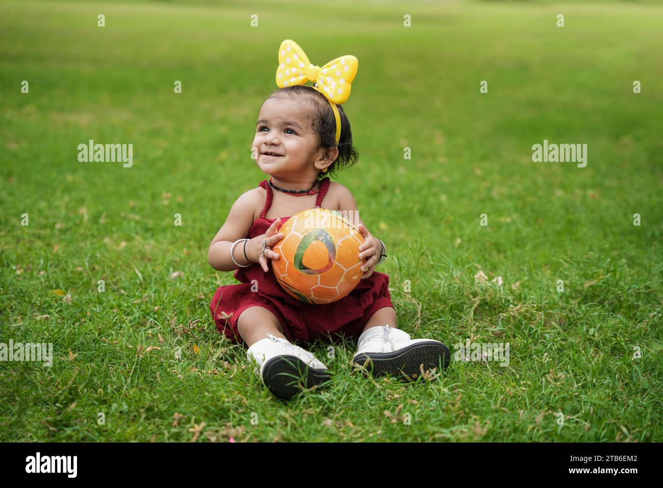 Belle petite fille indienne assise dans la pelouse du jardin et jouant avec la balle. Banque D'Images