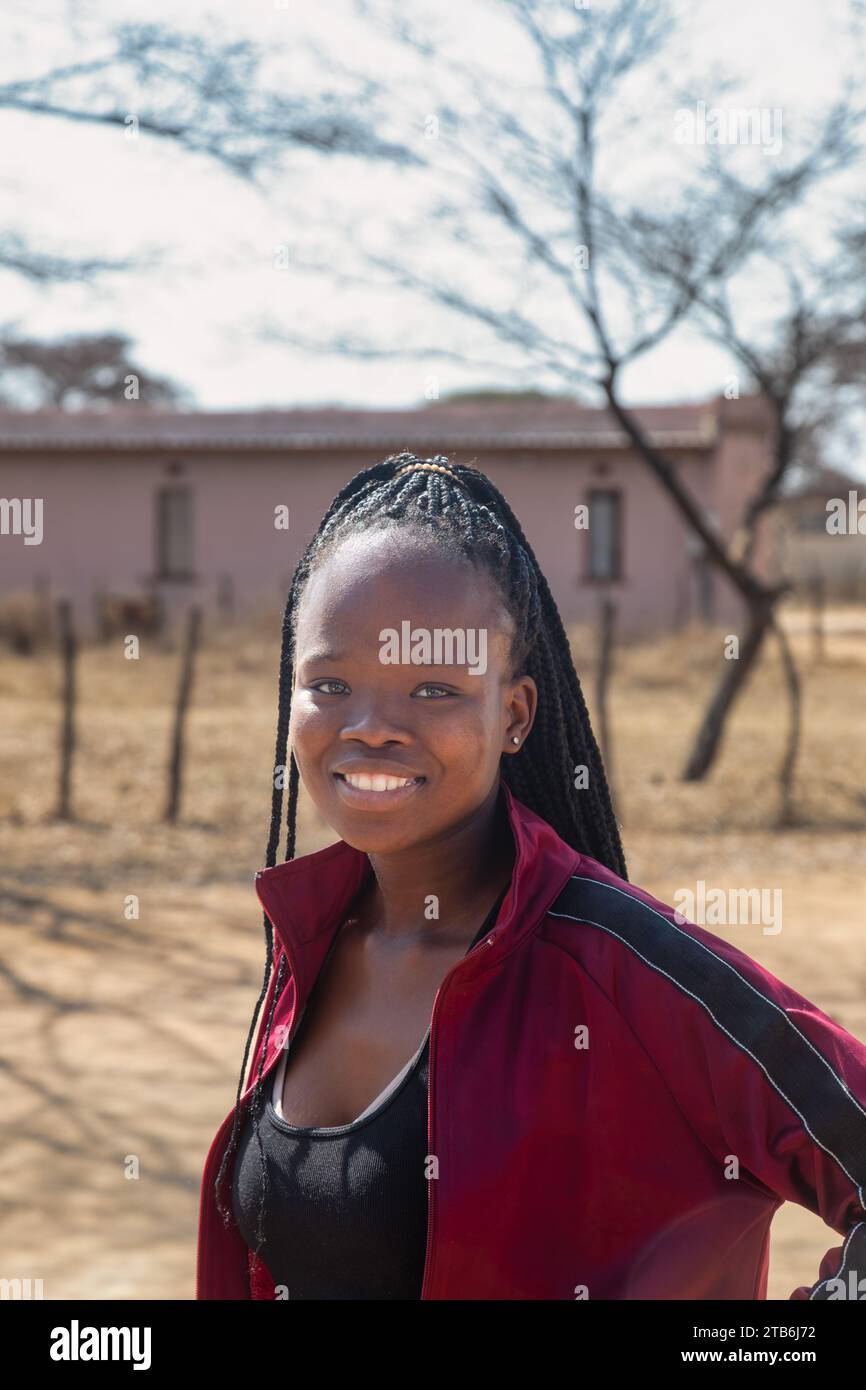 village, jeune fille africaine avec de longues tresses et un sourire toothy, maison de village en plein air Banque D'Images