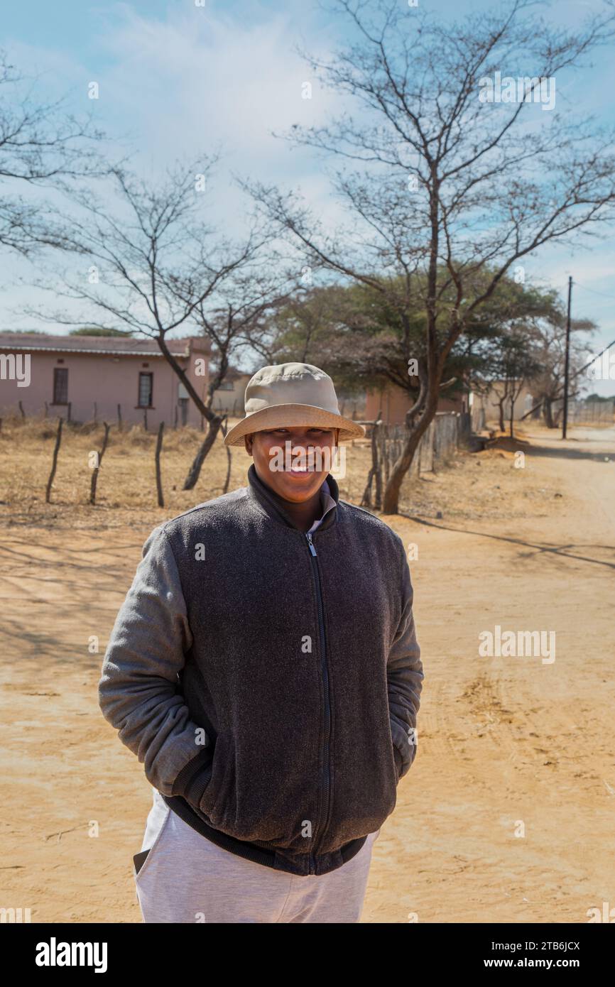 villageois , heureux en surpoids jeune homme africain avec un chapeau marchant sur un chemin de terre dans le village Banque D'Images