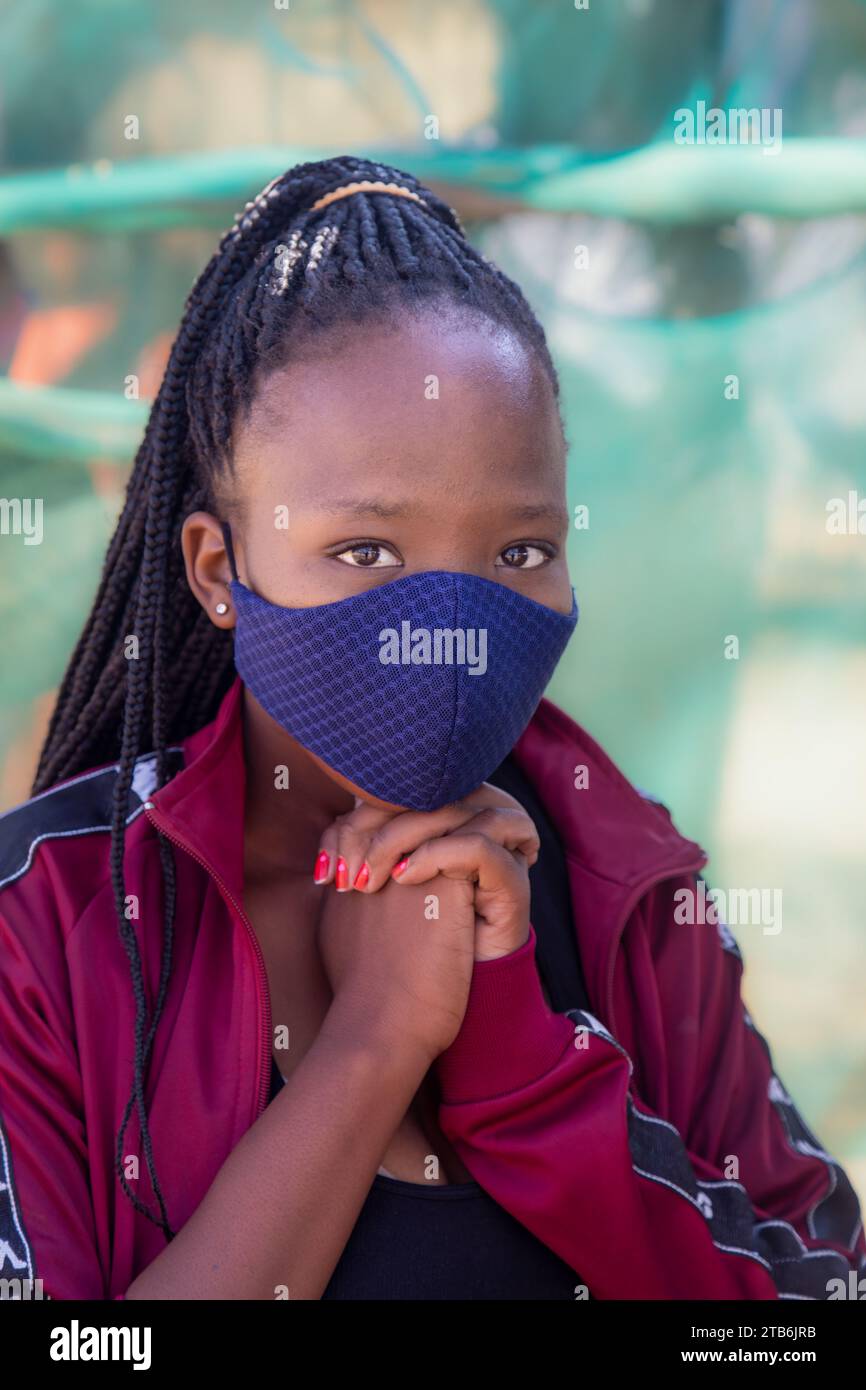 village, jeune fille africaine avec de longues tresses, portant un masque textile, fond vert extérieur Banque D'Images
