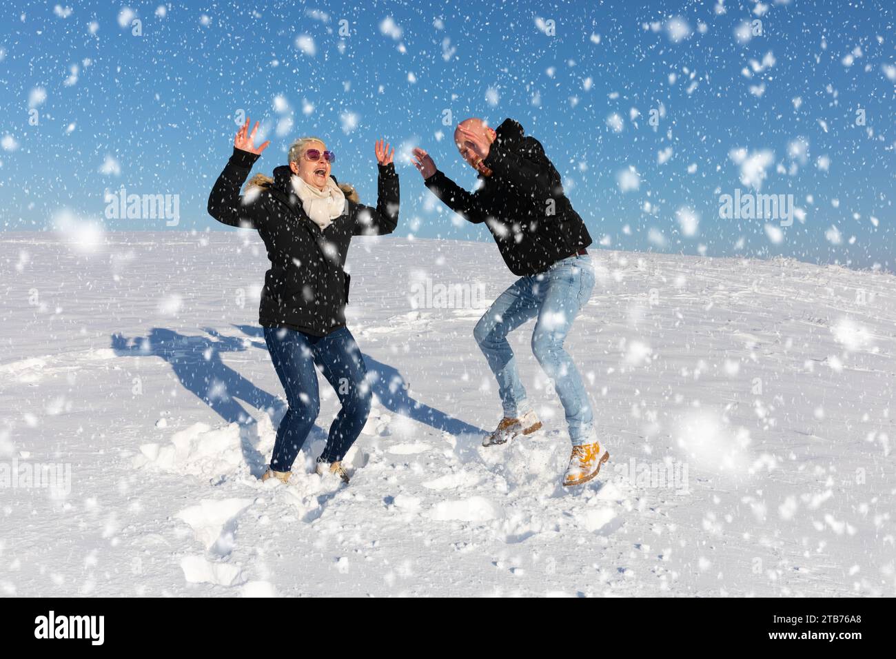 Un jeune couple, composé d'une femme et d'un homme, saute en l'air dans la neige et s'amuse ensemble Banque D'Images