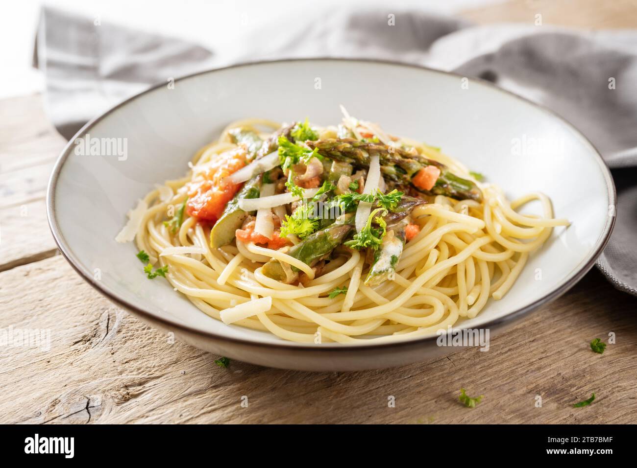 Spaghetti à la sauce aux légumes d'asperges vertes et tomates avec parmesan et garniture de persil dans une assiette sur une table en bois rustique, foyer sélectionné, Banque D'Images