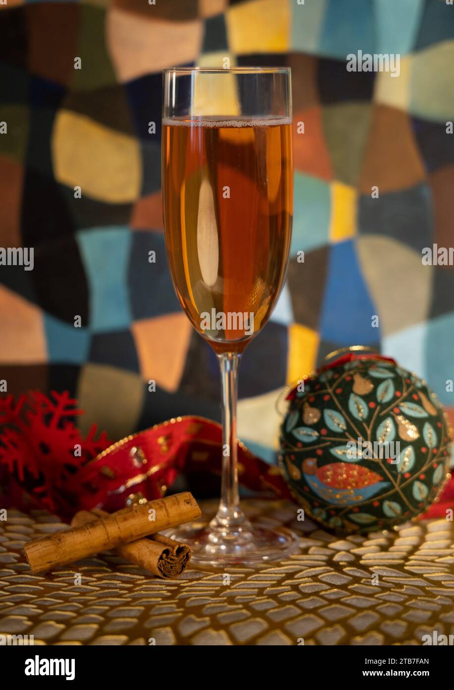 Grand verre de champagne avec décorations de Noël comprenant deux bâtonnets de cannelle, une boule verte, un flocon de neige rouge devant un tableau Banque D'Images