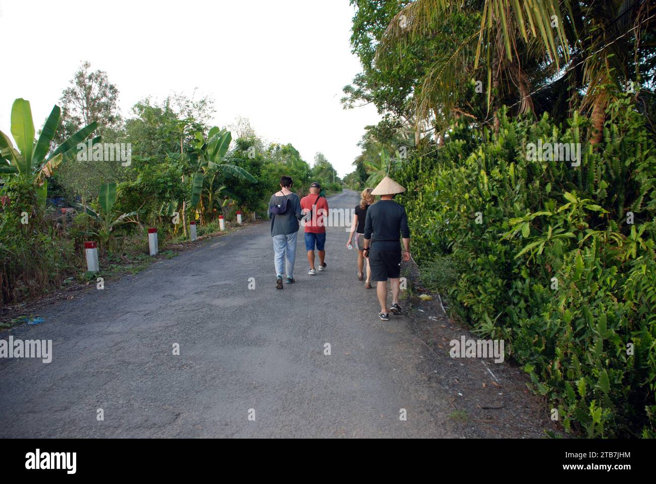 Les touristes et les populations locales marchent le long d'une route rurale dans la région du delta du Mékong au Sud Vietnam Banque D'Images