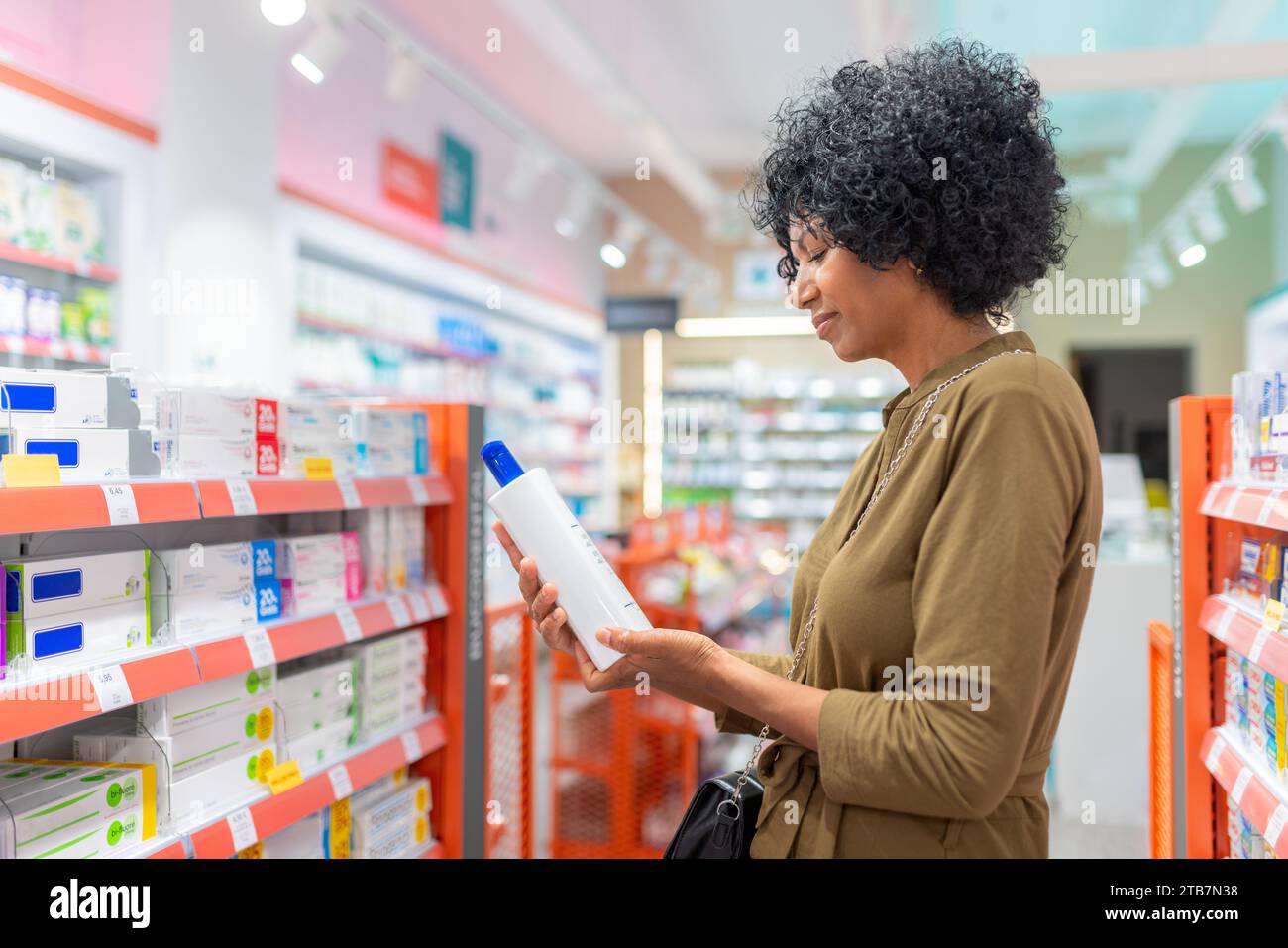 Vue latérale de la jeune femme noire tenant le flacon et vérifiant les informations sur l'étiquette du produit prescrit dans la pharmacie Banque D'Images