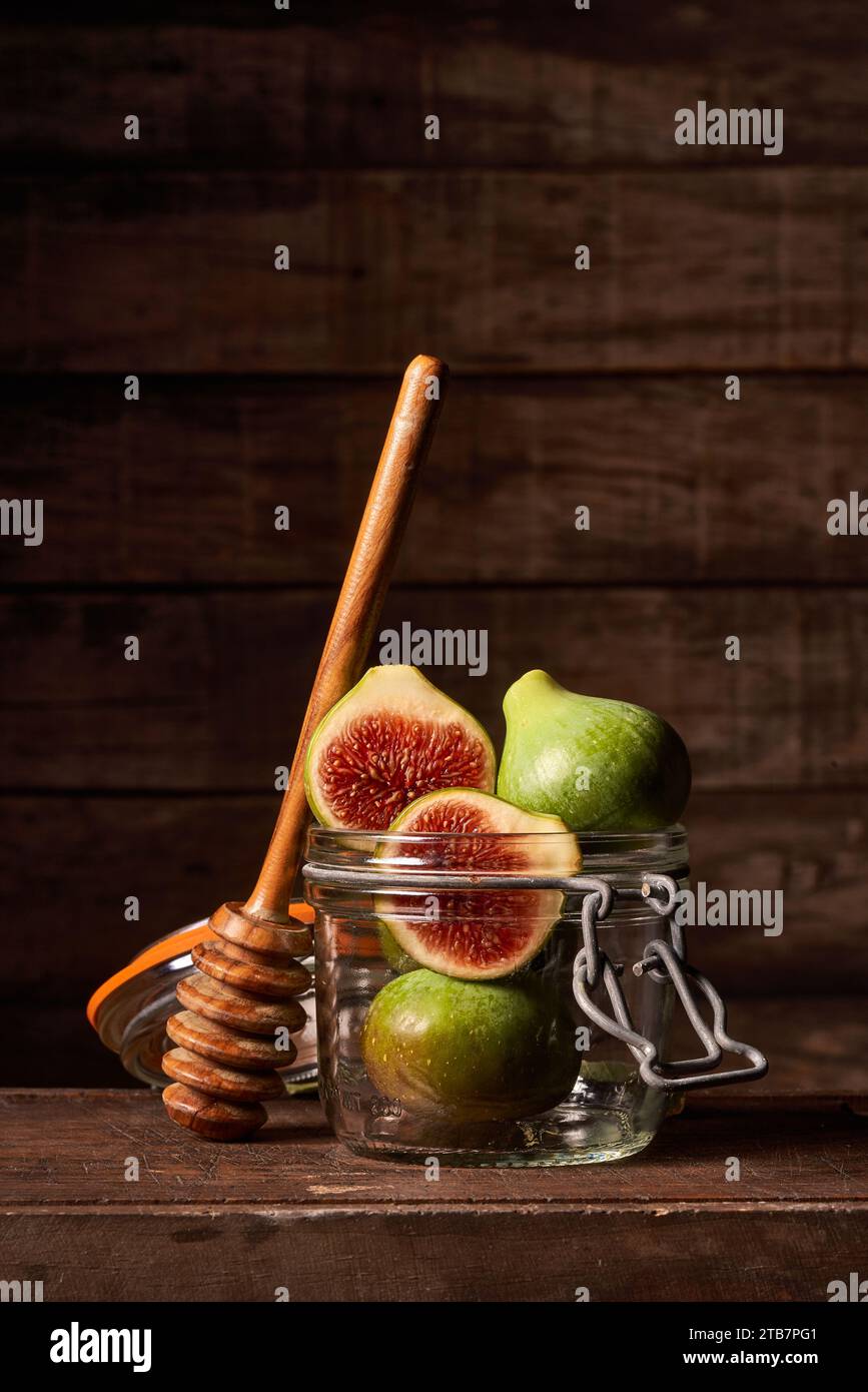 Figues entières et tranchées dans un bocal en verre avec un godet à miel en bois sur un fond de bois rustique, créant une sensation naturelle et saine. Banque D'Images