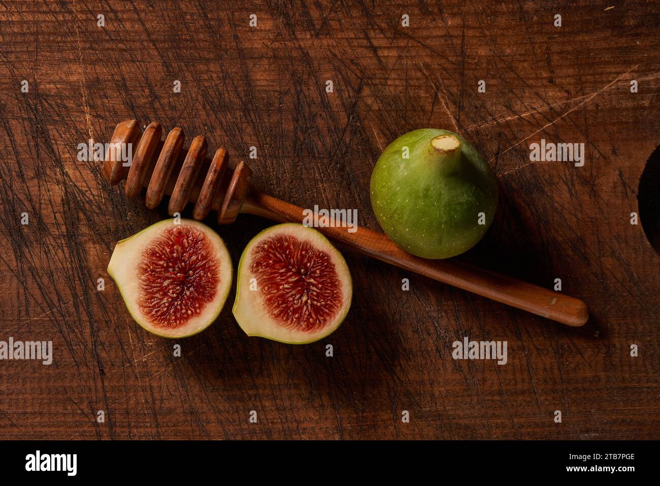 « Une vue de haut en bas de figues mûres à côté d'une pelle à miel sur une vieille surface en bois texturé, évoquant le charme culinaire rustique. » Banque D'Images