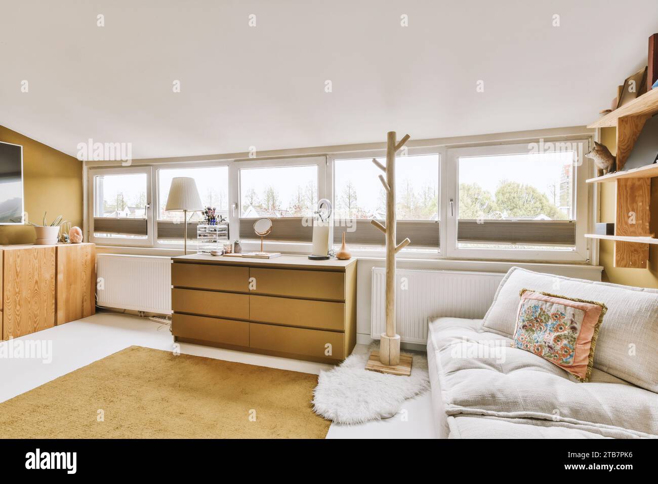 Canapé confortable avec des produits de beauté sur commode en bois placé par de grandes fenêtres lumineuses dans le salon moderne Banque D'Images