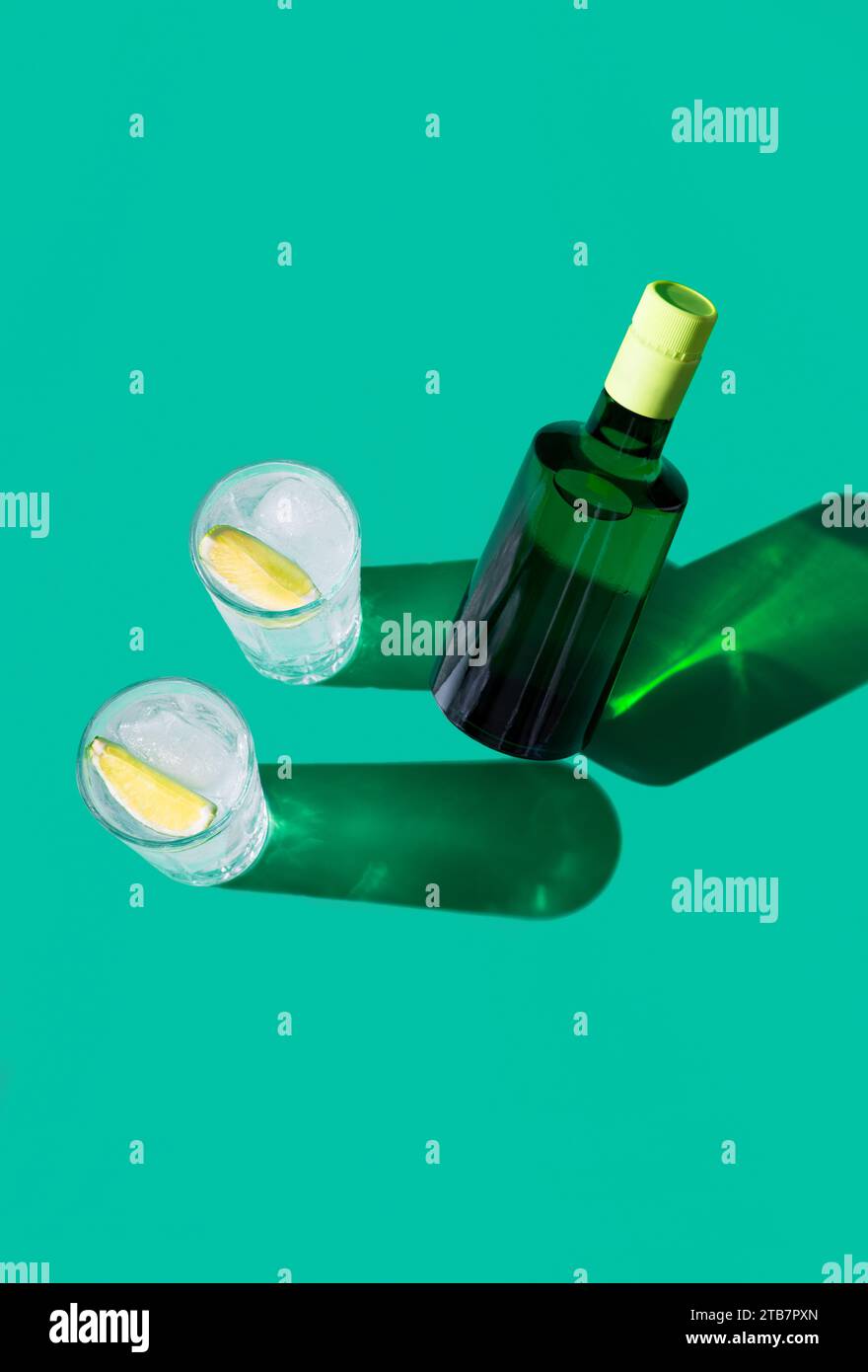 Un cocktail gin tonic élégant dans un verre avec une tranche de citron vert, mis en valeur sur un fond vert avec des ombres vives. Banque D'Images