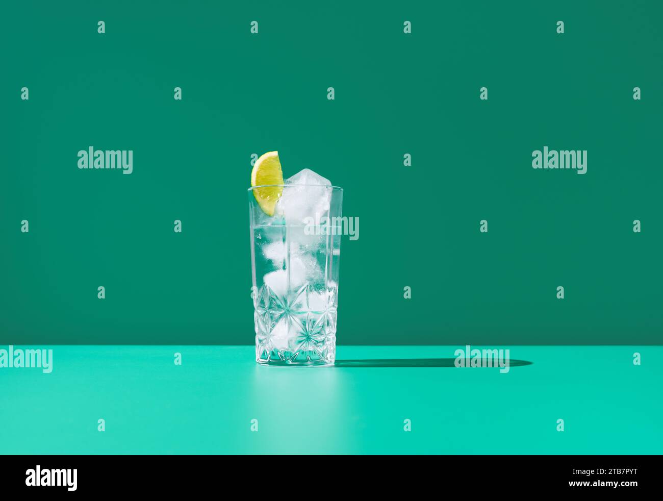 Un verre clair plein de gin tonic et recouvert d'une tranche de citron vert se trouve sur un fond vert vibrant, créant un visuel frais et frais. Banque D'Images