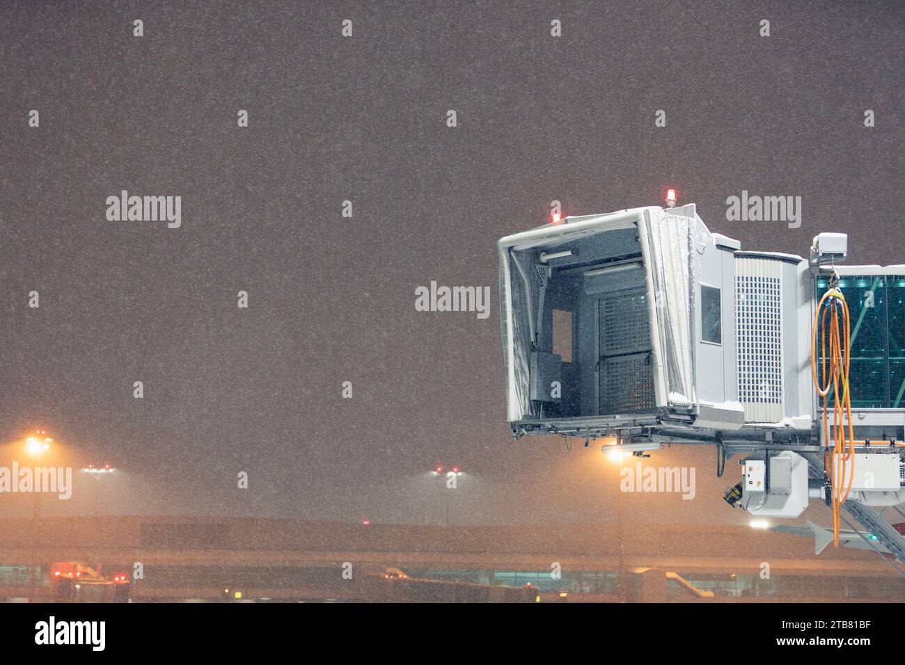 Hiver nuit glaciale à l'aéroport lors de fortes chutes de neige. Pont d'embarquement de passagers vide illuminé contre le ciel sombre avec des flocons de neige. Banque D'Images