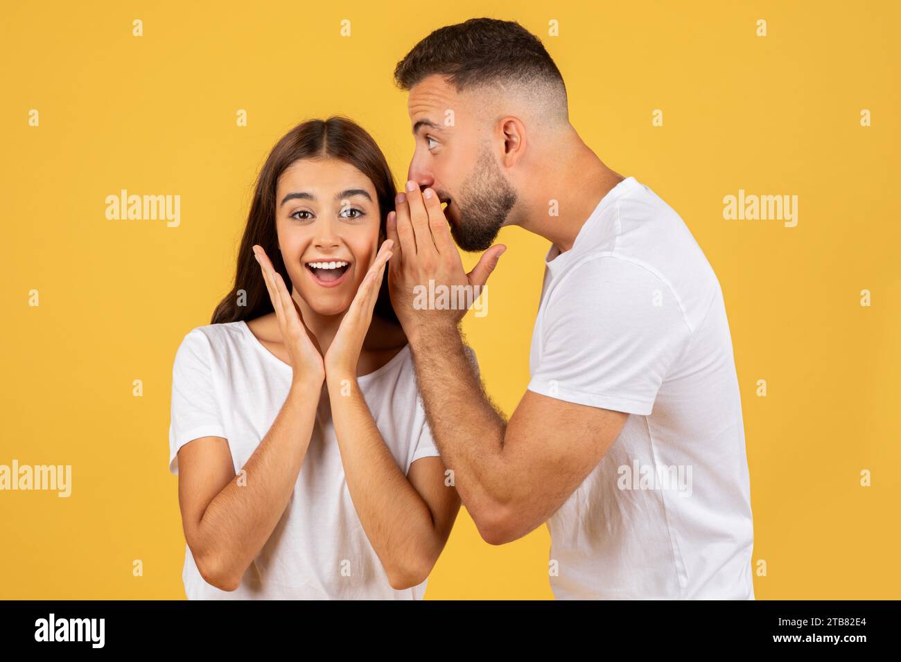 Heureux jeune homme européen en t-shirt blanc murmure à l'oreille de dame surprise secret Banque D'Images