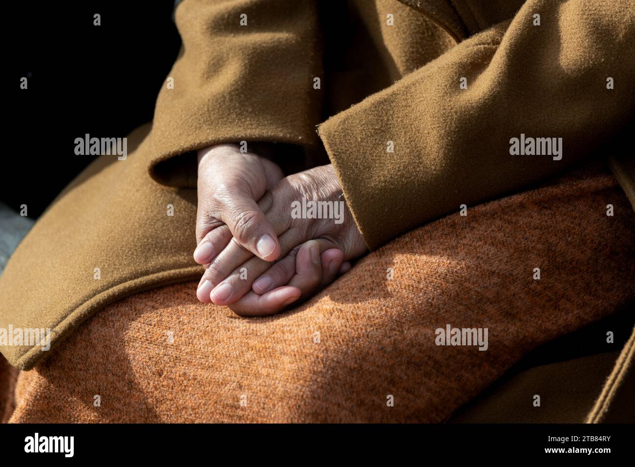 Les mains d'une femme sont serrées avec les doigts entrelacés et couchées doucement dans une pose calme et détendue sur ses genoux. Banque D'Images