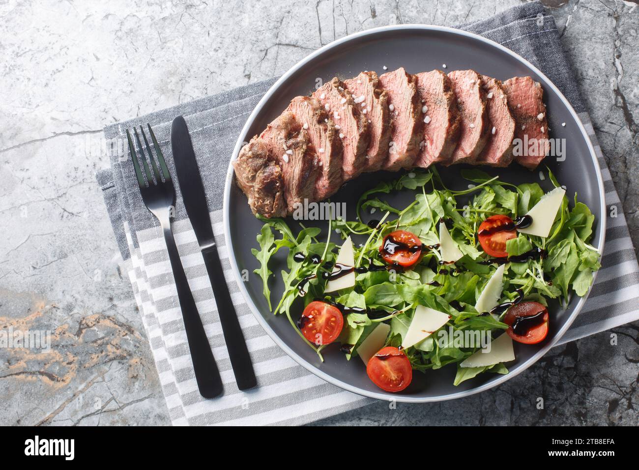 Plat principal italien traditionnel tagliata de bœuf Steak tendre, roquette, tomates cerises, copeaux de Grana Padano, réduction balsamique gros plan sur une assiette sur t Banque D'Images