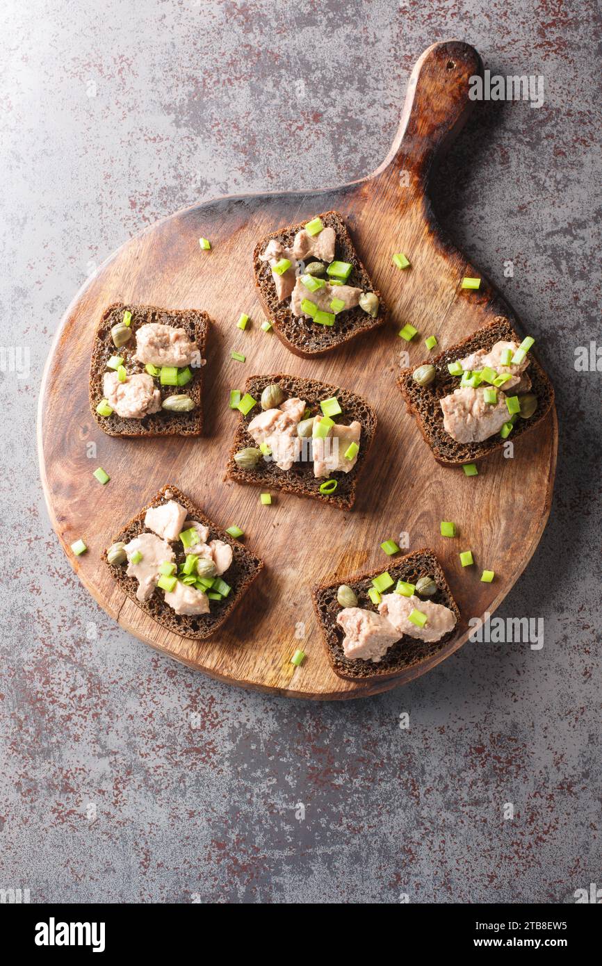 Sandwichs avec foie de morue en conserve, oignons verts et câpres gros plan sur une planche de bois sur la table. Vue verticale de dessus Banque D'Images