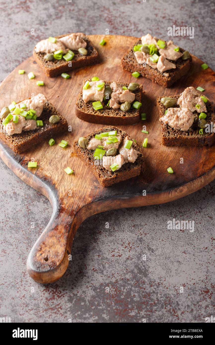 Sandwichs avec foie de morue en conserve, oignons verts et câpres gros plan sur une planche de bois sur la table. Vertical Banque D'Images