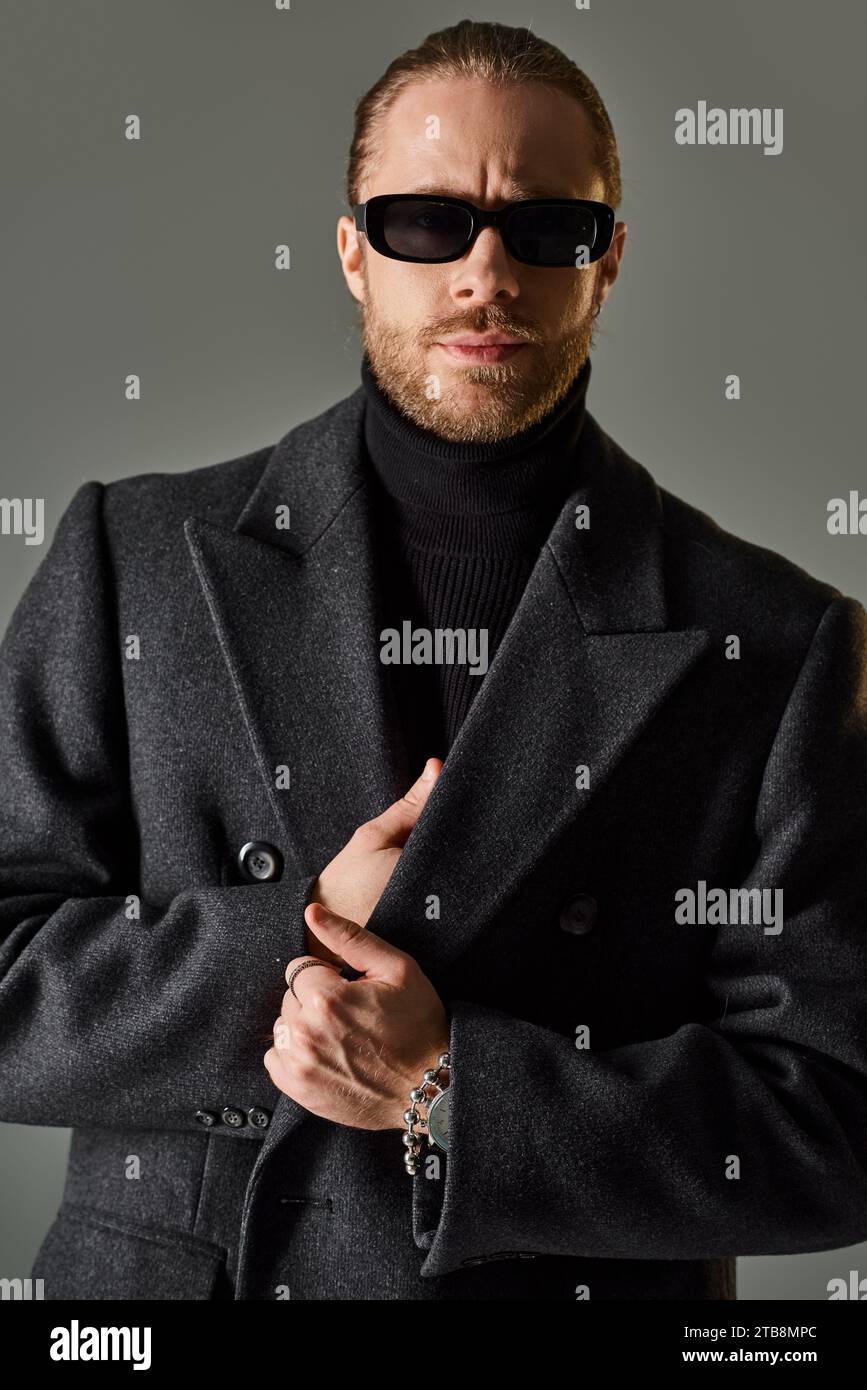 portrait de beau modèle masculin dans des lunettes de soleil à la mode et tenue noire debout sur fond gris Banque D'Images