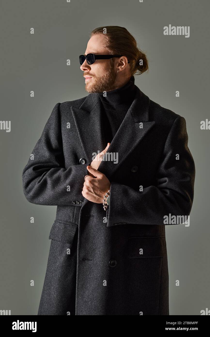 portrait de beau modèle masculin dans des lunettes de soleil à la mode et tenue noire regardant loin sur fond gris Banque D'Images