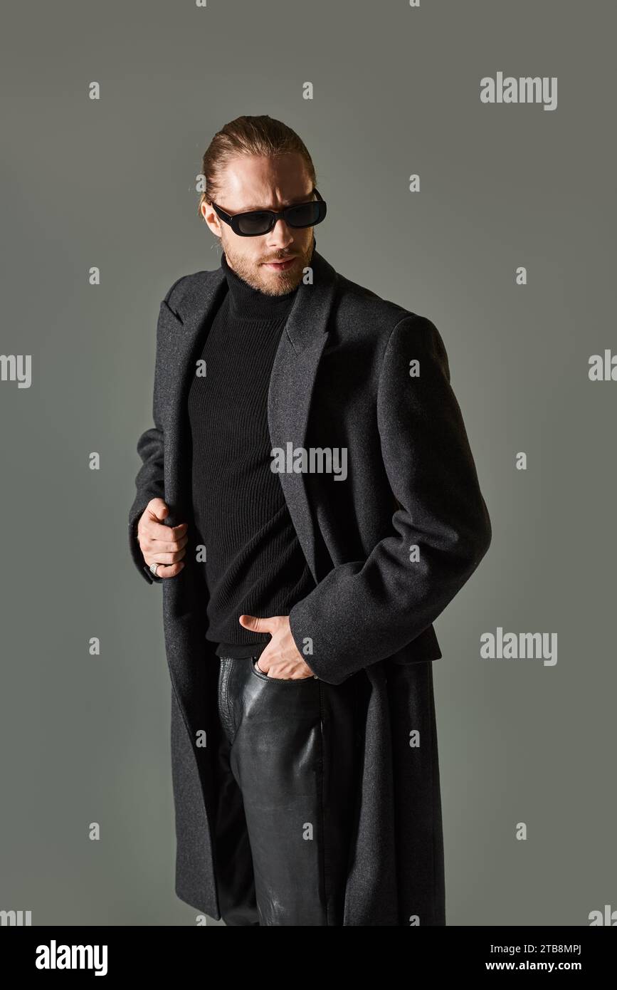 portrait de beau modèle masculin dans des lunettes de soleil à la mode et tenue noire posant avec la main dans la poche Banque D'Images