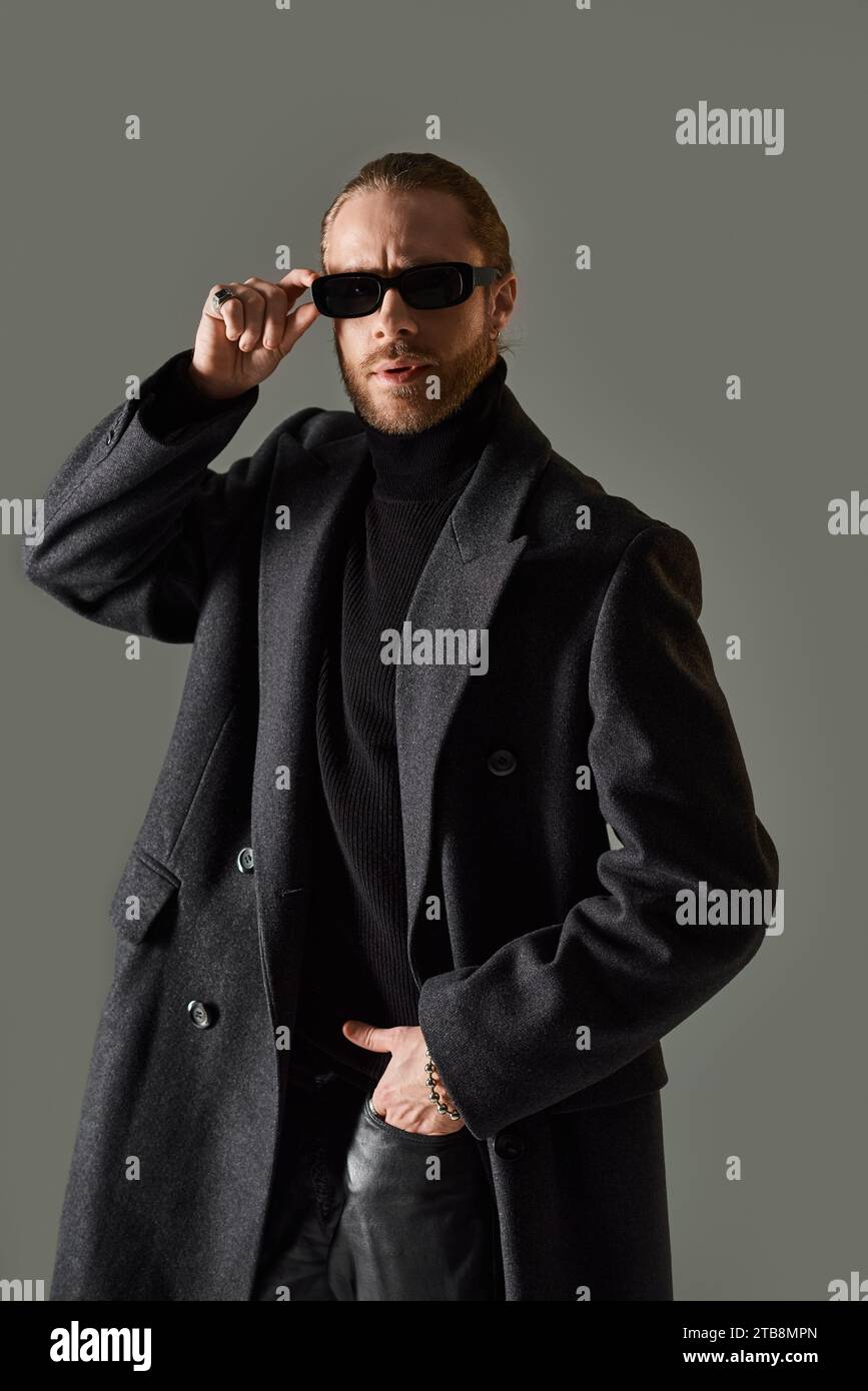 portrait de beau modèle masculin dans des lunettes de soleil à la mode et tenue noire posant avec la main dans la poche Banque D'Images