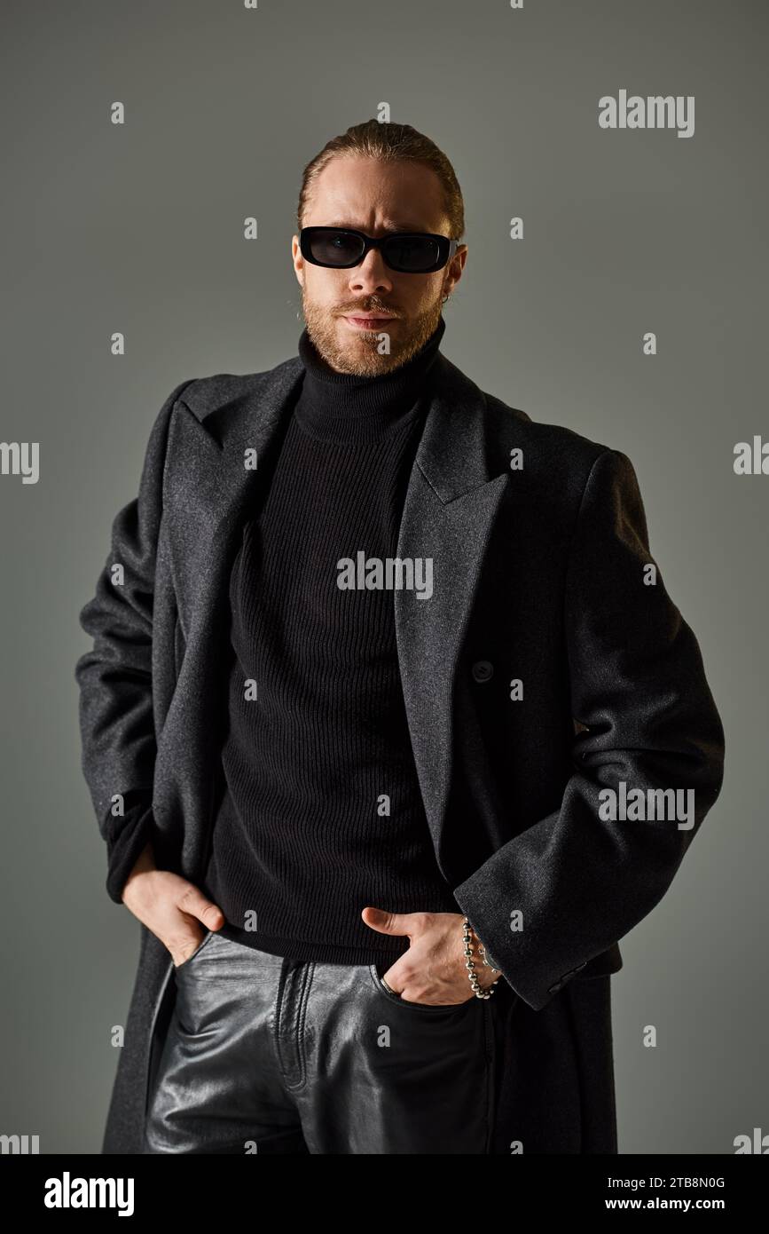 portrait de beau modèle masculin dans des lunettes de soleil à la mode et tenue noire debout avec les mains dans les poches Banque D'Images