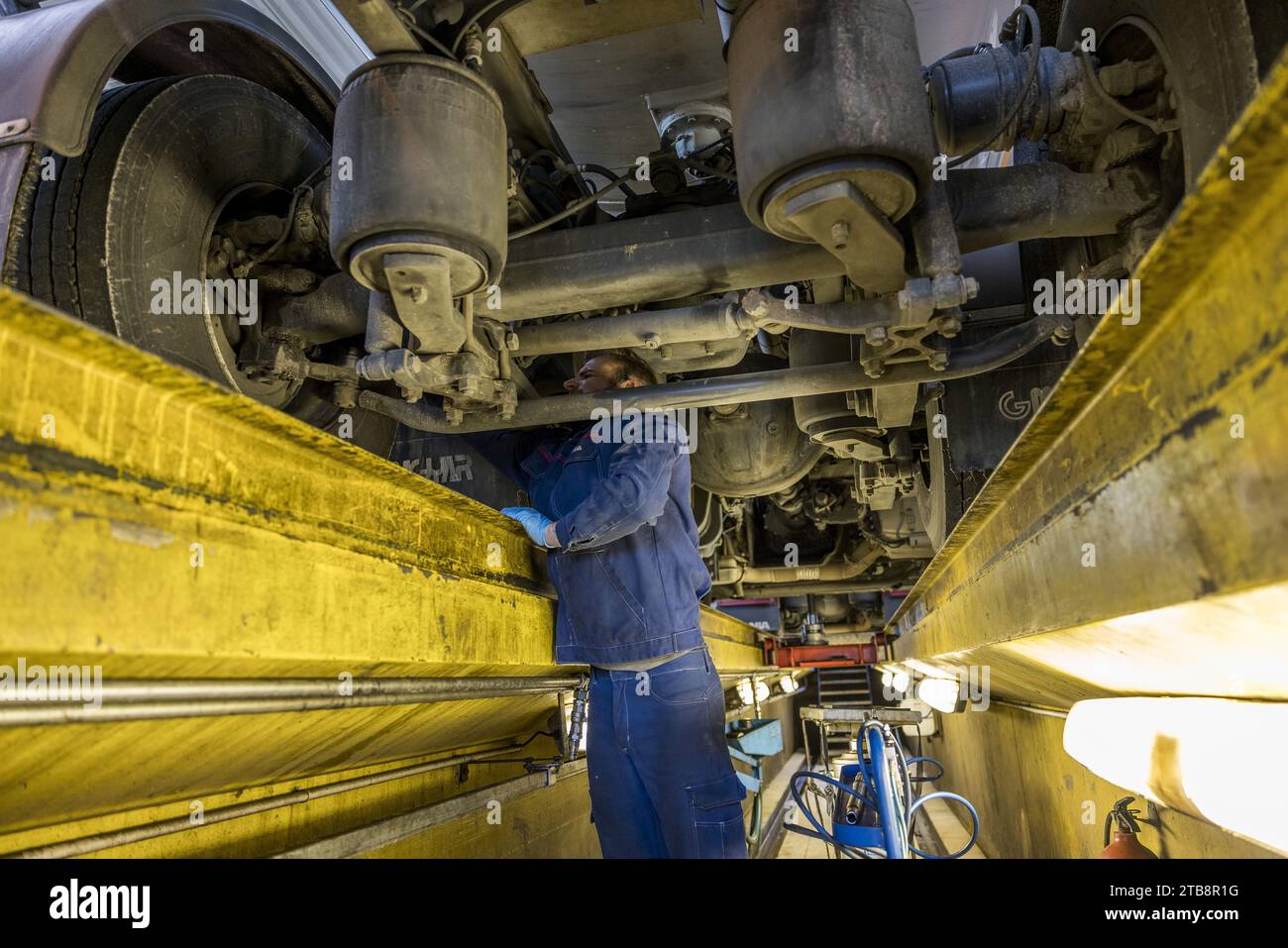 Garage, atelier de réparation pour poids lourds : mécanicien dans la fosse d'inspection travaillant sur le moteur d'un camion Scania Banque D'Images