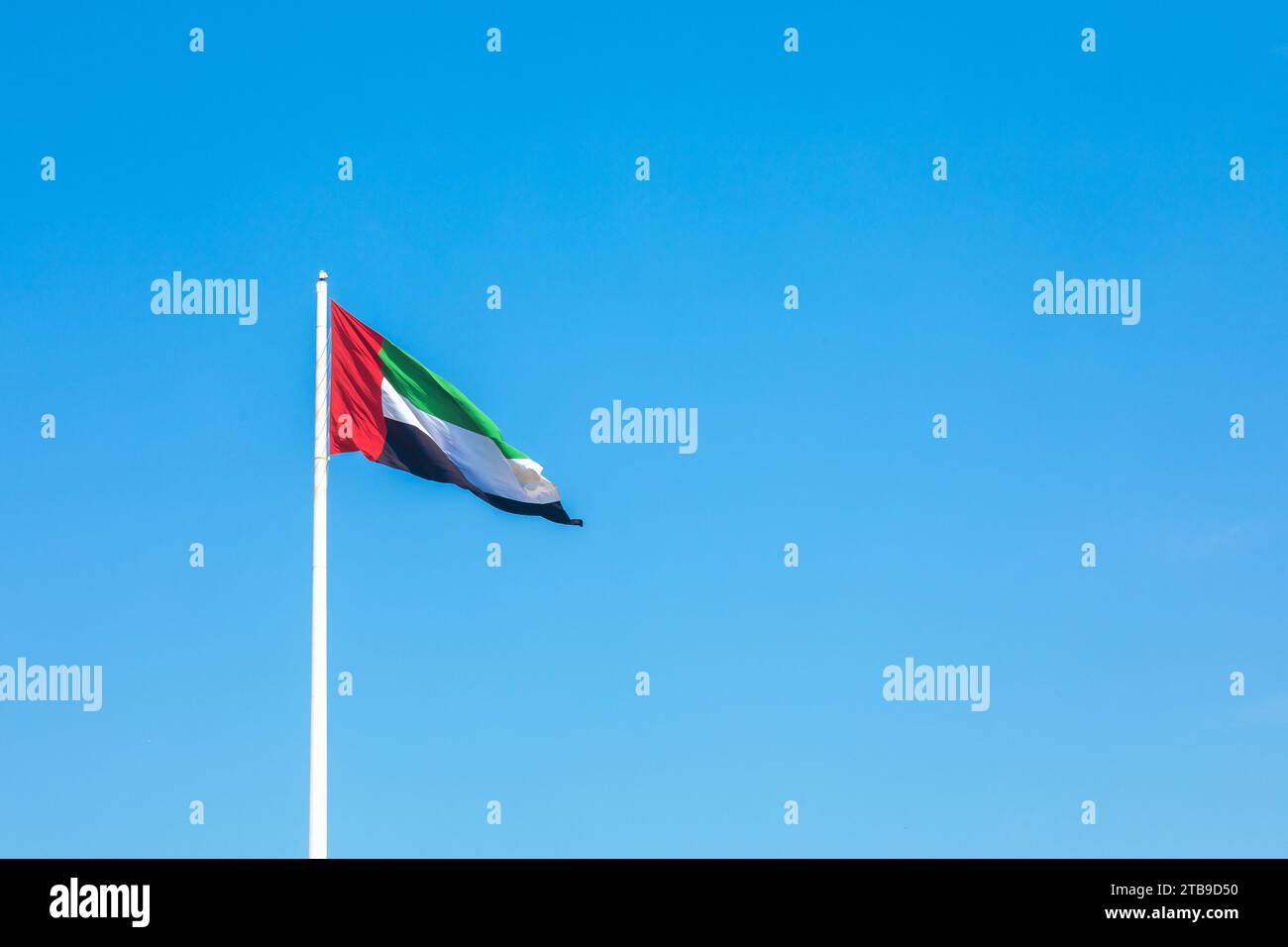 Agitant le drapeau des Émirats arabes Unis sur un mât contre un ciel bleu Banque D'Images