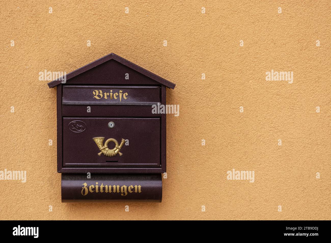 Boîte aux lettres brune avec un emblème sur un fond d'un mur orangé plâtré avec des lettres dorées. Traduction : 'lettres', 'journals'. Banque D'Images