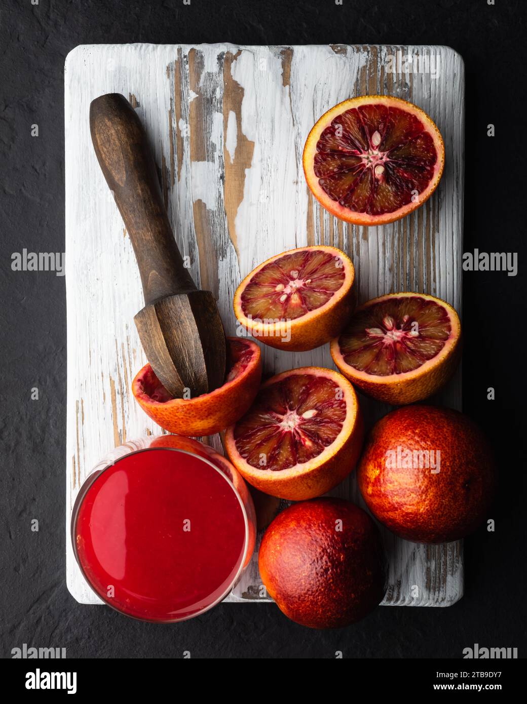 Morceaux d'oranges siciliennes rouges et presse-étoupe à main sur panneau de bois blanc closeup. Concept vitaminique d'alimentation saine. Photographie culinaire Banque D'Images
