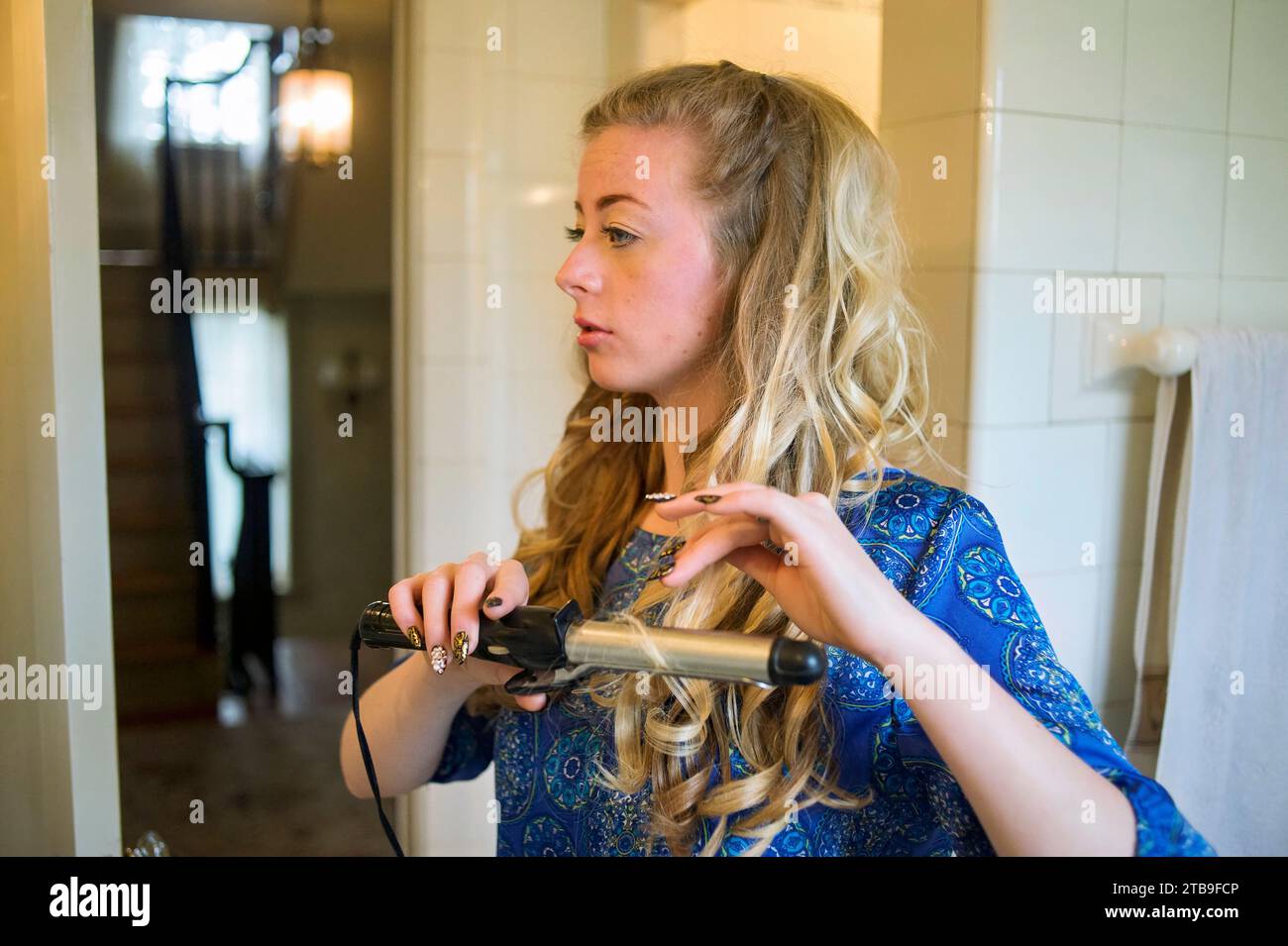 Adolescente boucle ses longs cheveux blonds alors qu'elle se prépare pour son bal senior ; Lincoln, Nebraska, États-Unis d'Amérique Banque D'Images