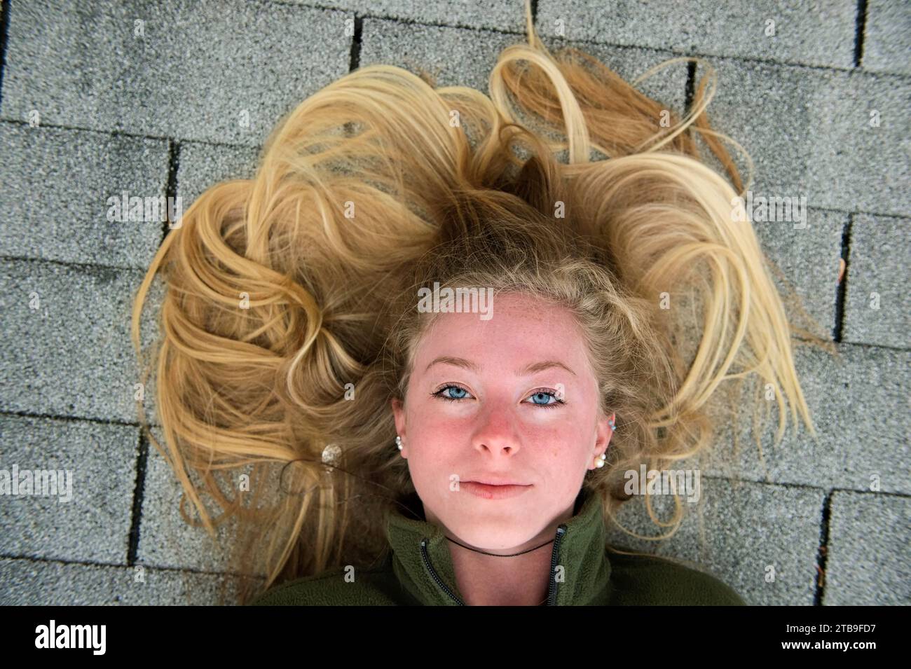 Adolescente aux longs cheveux blonds repose sur un toit en bardeaux ; Elkhorn, Nebraska, États-Unis d'Amérique Banque D'Images