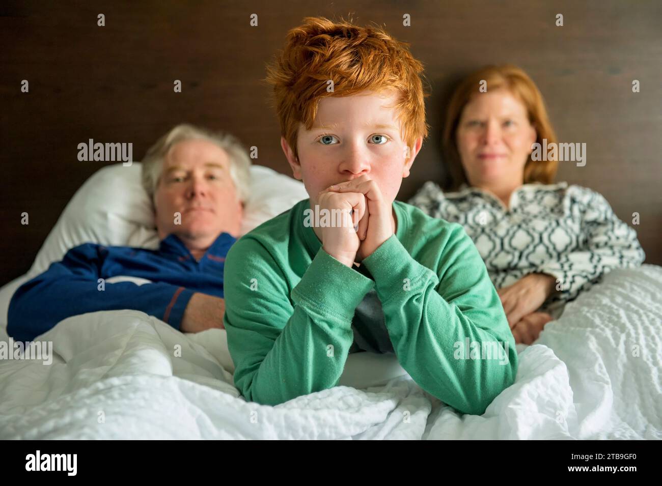 Jeune garçon dans un lit avec ses parents, ayant un regard craintif sur son visage ; Omaha, Nebraska, États-Unis d'Amérique Banque D'Images