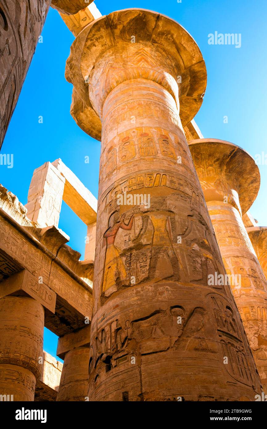 Vue rapprochée des hiéroglyphes sur les colonnes de la Grande salle hypostyle, atteignant vers le ciel bleu dans le complexe du temple de Karnak près de L... Banque D'Images