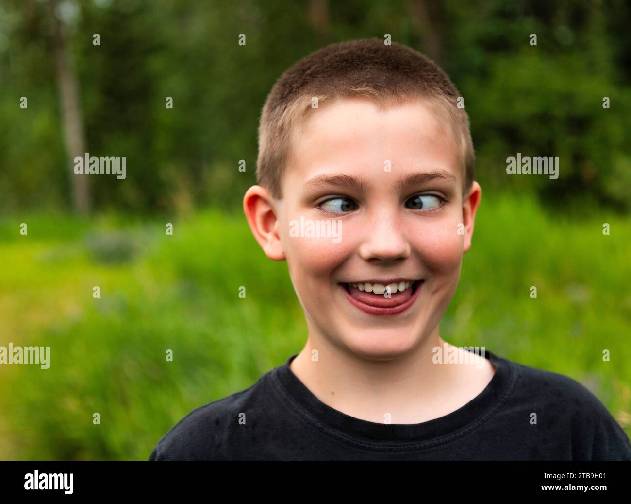 Portrait rapproché d'un garçon croisant les yeux et faisant un visage drôle tout en se tenant debout dans une forêt ; Edmonton, Alberta, Canada Banque D'Images