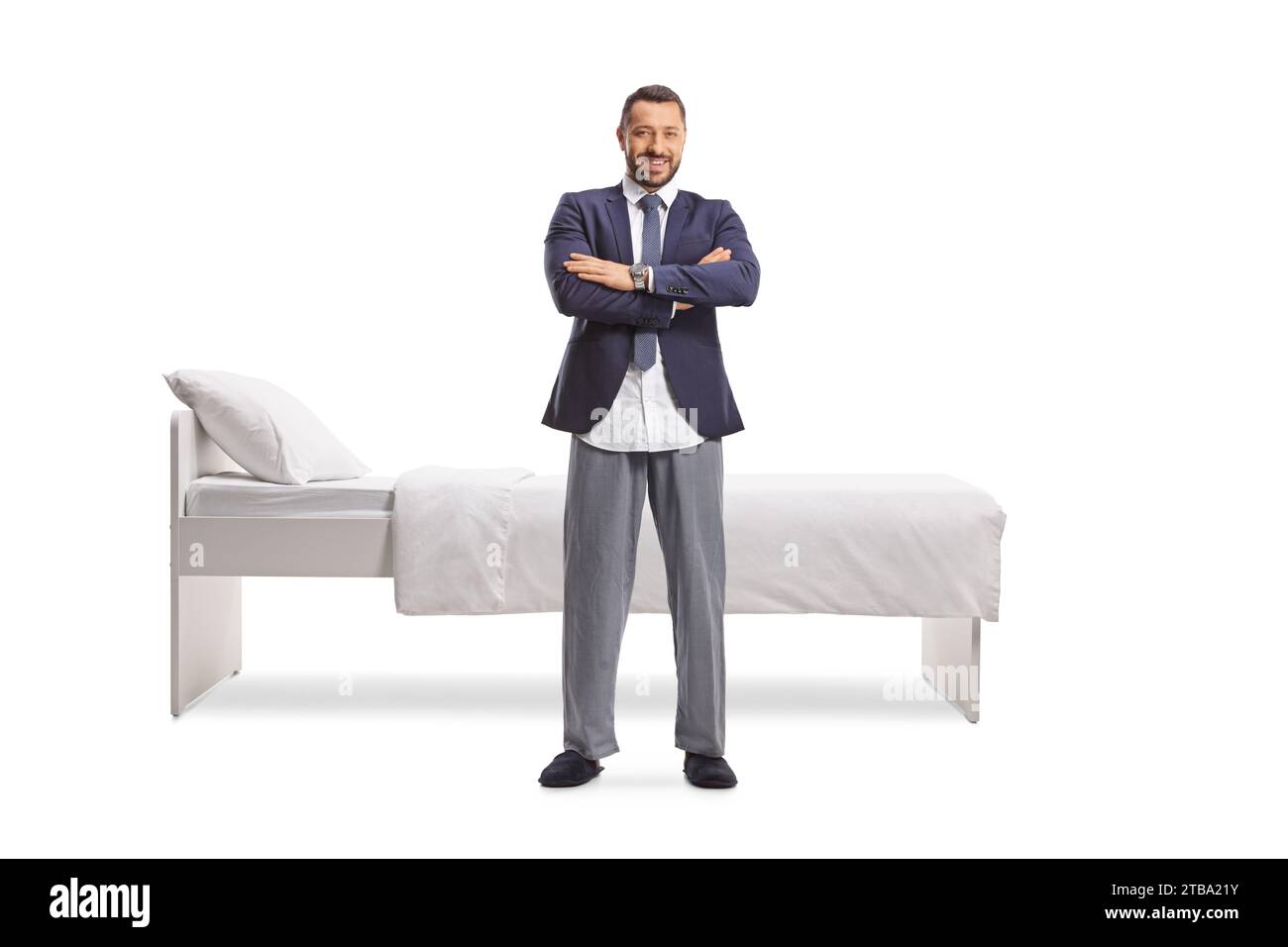 Portrait en longueur d'un homme d'affaires dans un costume et pyjama inférieur debout devant un lit isolé sur fond blanc Banque D'Images Portrait en longueur d'un homme d'affaires dans un costume et pyjama inférieur debout devant un lit isolé sur fond blanc Banque D'Images