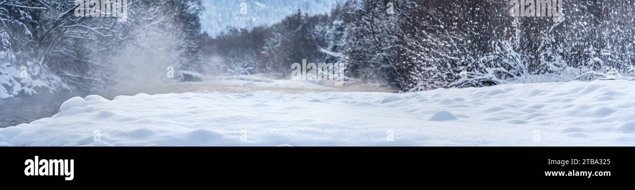 Rivière froide d'hiver, vapeur visible au-dessus de l'eau, arbres sombres des deux côtés, rivage couvert de neige fraîche au premier plan - large panorama Banque D'Images