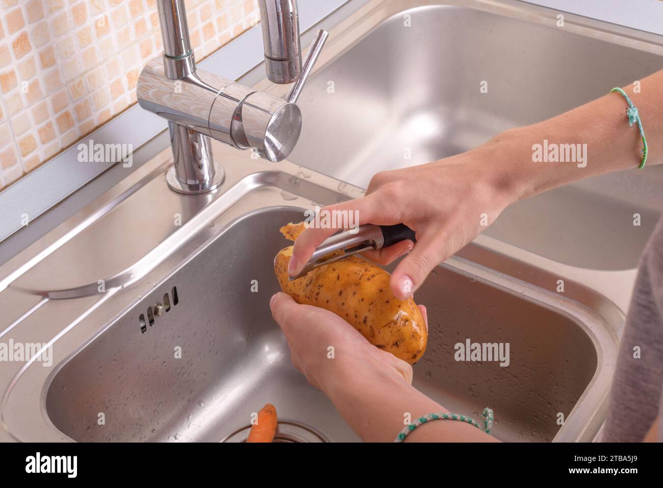 Mains féminines épluchant une pomme de terre dans l'évier dans la cuisine. Légumes, végétariens, préparation pour la cuisine, aliments sains, mode de vie alimentaire Banque D'Images